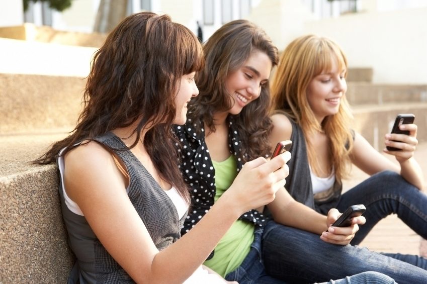 Group Of Teenage Students Sitting Outside On College Steps Using Mobile Phone Group Of Teenage Students Sitting Outside On College Steps Using Mobile Phone